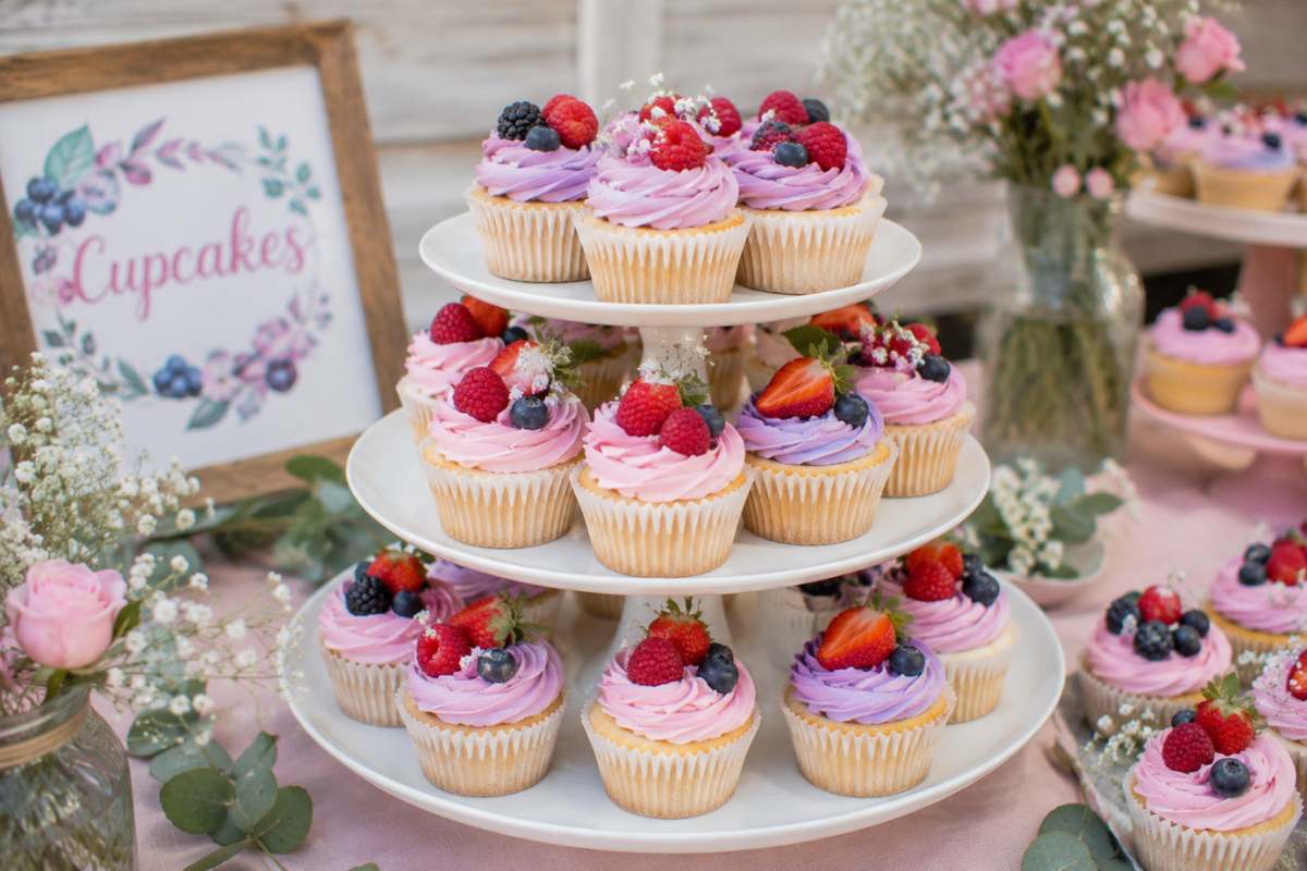 Beautiful berry cupcake dessert display featuring pastel frosted cupcakes, fresh strawberries and blueberries, tiered cake stands, and adorable berry-themed baby shower dessert ideas.