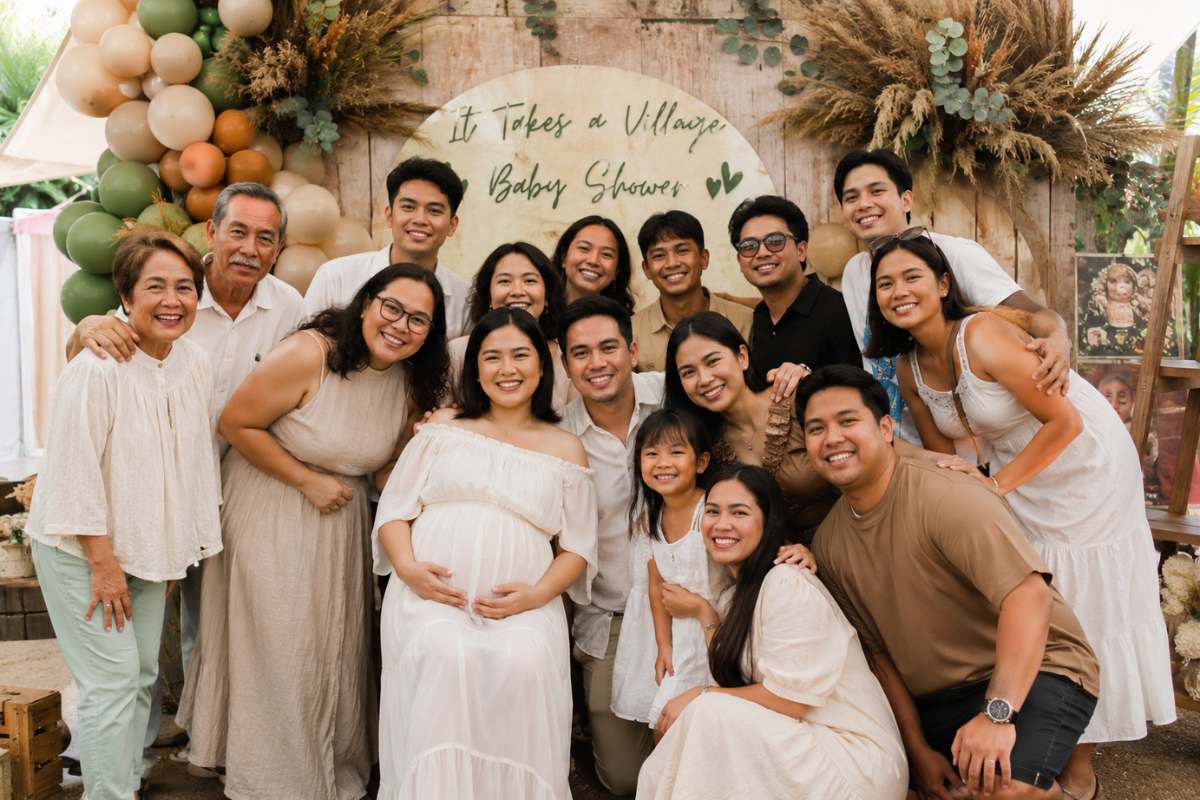 A heartwarming "It Takes a Village" baby shower group photo featuring a pregnant mom surrounded by family and friends in front of a rustic themed backdrop with balloons, pampas grass, and neutral-toned decor. This village-inspired baby shower photo area encourages group pictures that celebrate community, support, and togetherness as loved ones gather to welcome a new baby.
