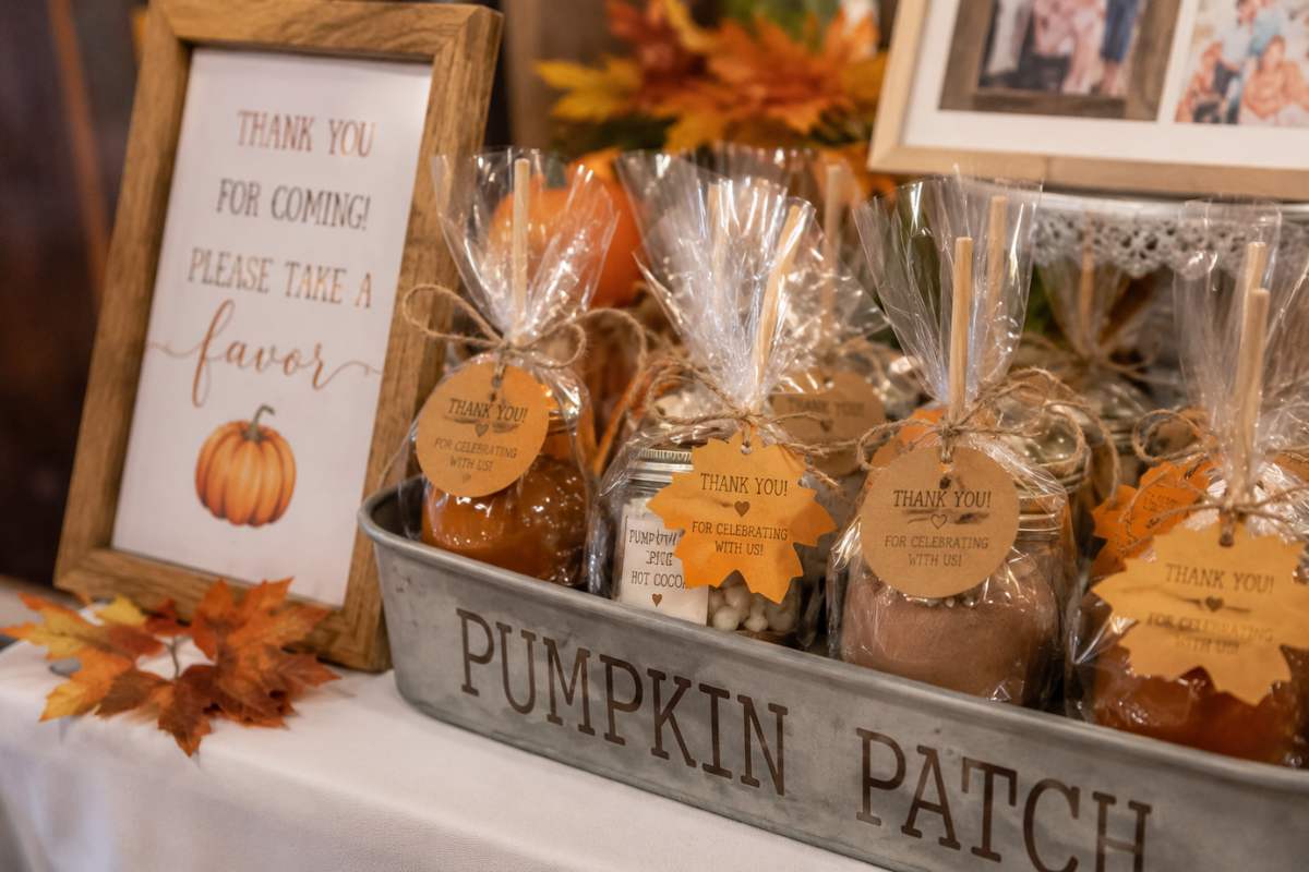 Pumpkin patch baby shower party favors featuring mini caramel apples, pumpkin spice hot cocoa jars, and seasonal treats wrapped in clear packaging with rustic twine and leaf-shaped thank-you tags displayed on a festive fall favor table.