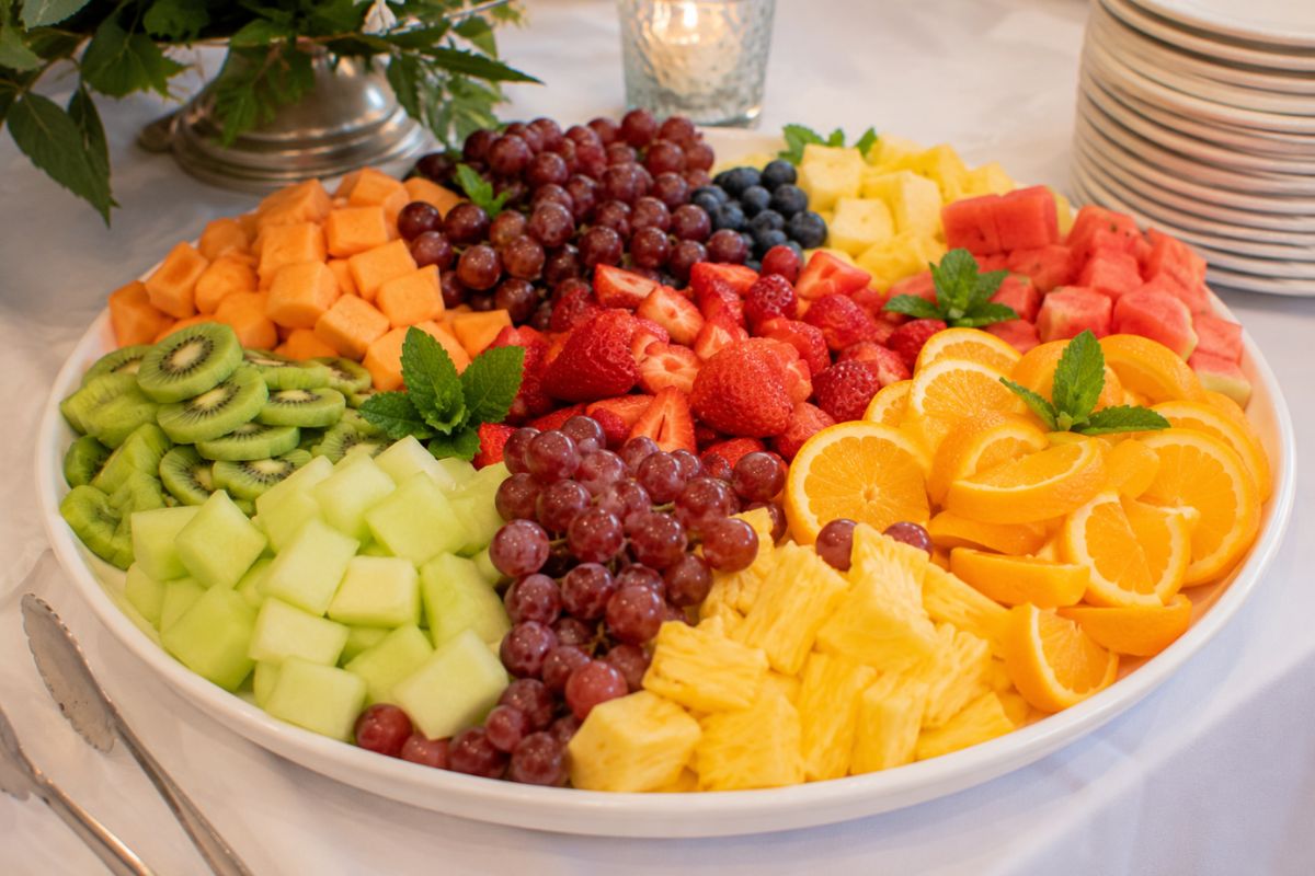 Fresh seasonal fruit platter with strawberries, grapes, pineapple, watermelon, cantaloupe, honeydew, kiwi, blueberries, and orange slices beautifully arranged on a large serving tray as a colorful and budget-friendly dessert for a wedding reception buffet.