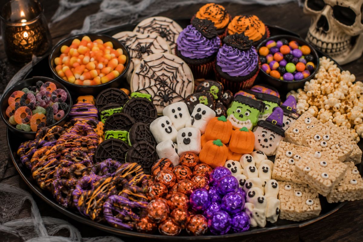 Halloween dessert platter filled with decorated cookies, chocolate-covered pretzels, marshmallow ghosts, candy corn, mini cupcakes, popcorn, chocolates, and festive sweets.