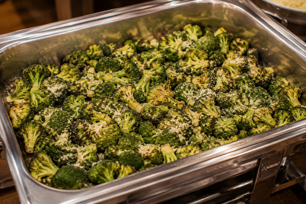 Parmesan roasted broccoli with crispy edges, garlic, Italian herbs, and grated Parmesan served in a stainless steel buffet chafing dish as an elegant and budget-friendly wedding reception side dish.