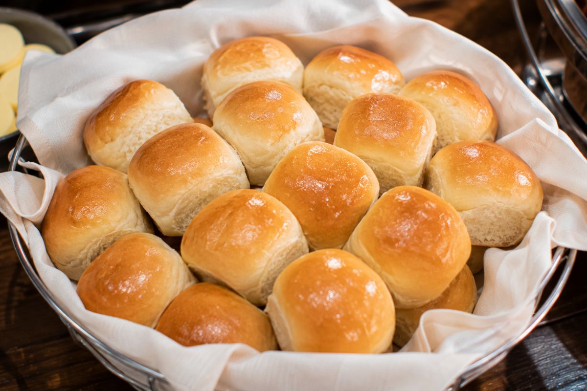 Soft golden dinner rolls served in a lined bread basket with whipped butter, offering a simple and elegant bread option for a wedding reception buffet.