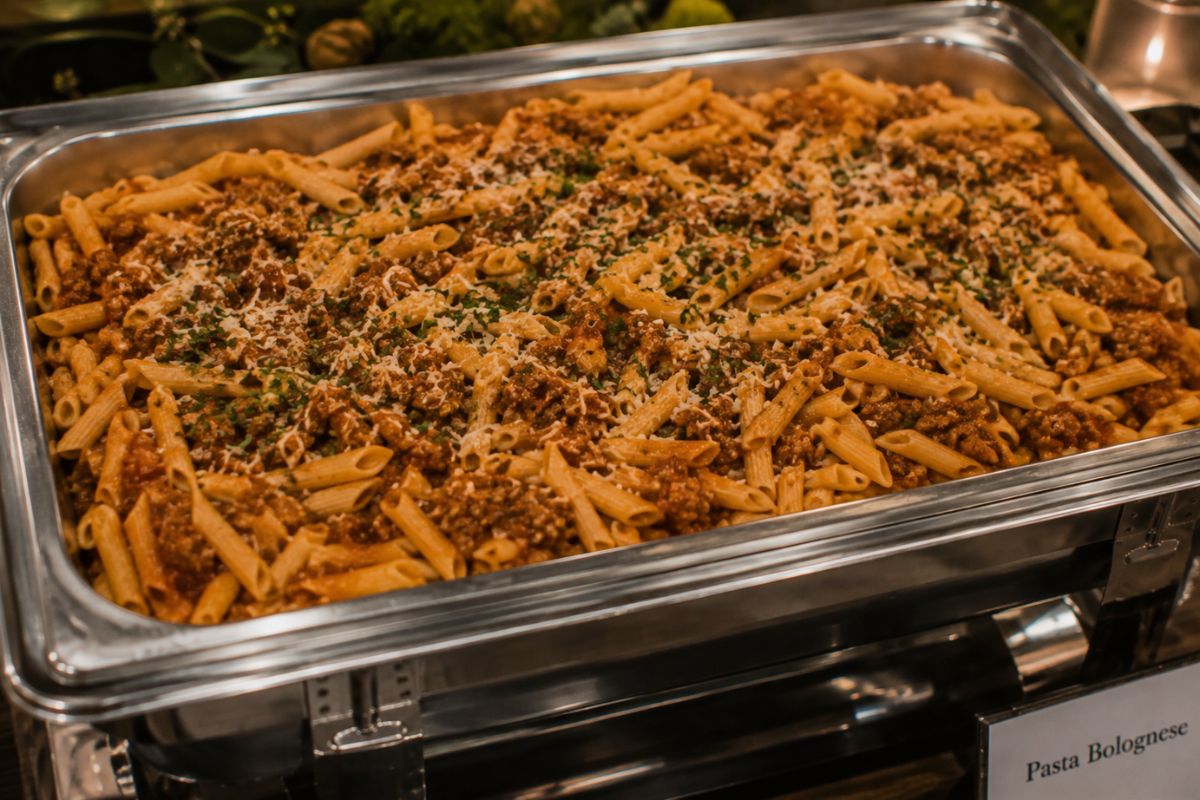 Traditional pasta Bolognese with slow-simmered meat sauce and grated Parmesan served in a buffet chafing dish, offering a hearty and budget-friendly wedding reception entrée.