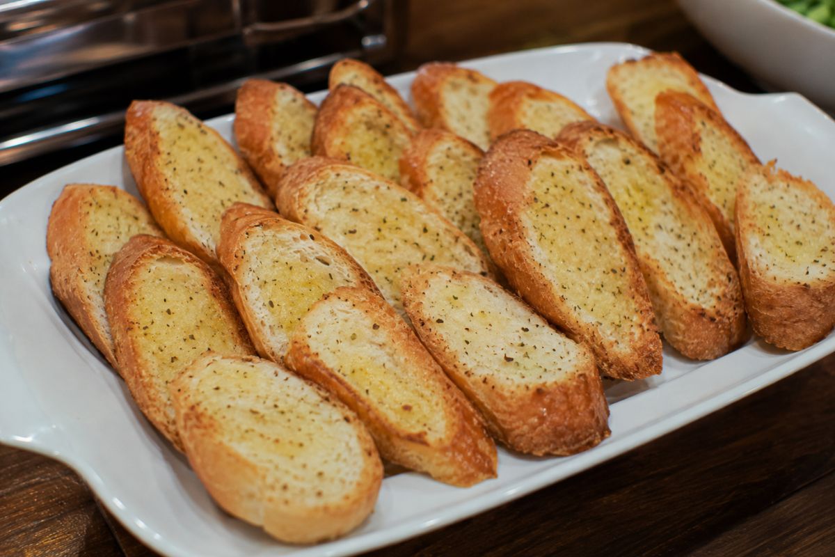 Warm garlic bread slices with buttery garlic spread and Italian herbs arranged on a serving platter, making an affordable and crowd-pleasing side dish for a wedding reception buffet.