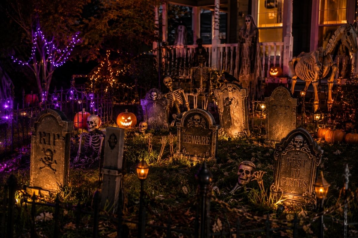 Classic Halloween front yard graveyard with tombstones, skeletons, pumpkins, faux fencing, lanterns, and purple and warm lighting