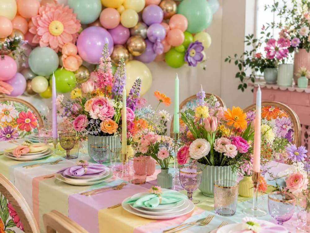 Colorful party table decorated with bold pastel shades of mint green, lilac, peach, and yellow, featuring vibrant floral centerpieces, oversized flower accents, pastel balloon backdrop, gold flatware, and elegant spring-inspired table settings.