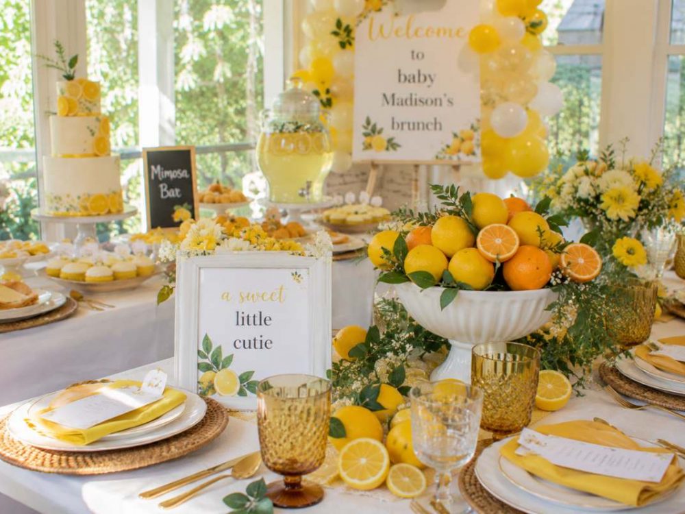 Citrus-themed brunch baby shower décor featuring lemons, oranges, yellow floral arrangements, balloon accents, citrus centerpieces, and elegant brunch table settings in a bright sunlit venue.