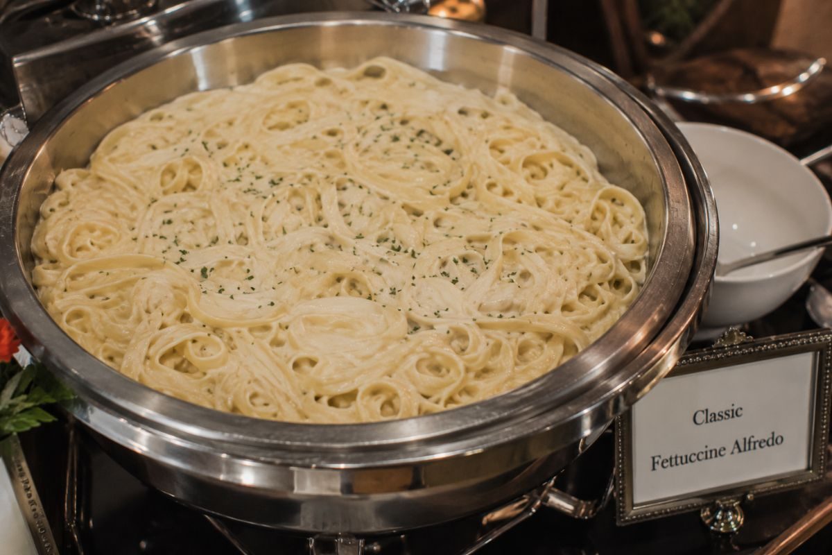 Classic fettuccine Alfredo with creamy Parmesan sauce served in an elegant buffet chafing dish, making a comforting and affordable wedding reception pasta entrée.
