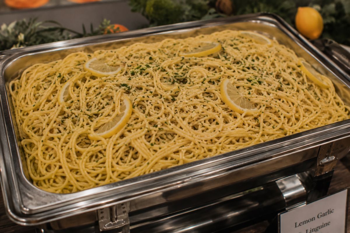 Lemon garlic linguine with fresh lemon slices, Parmesan cheese, parsley, and herbs served in a buffet chafing dish, perfect for a light spring or summer wedding reception.