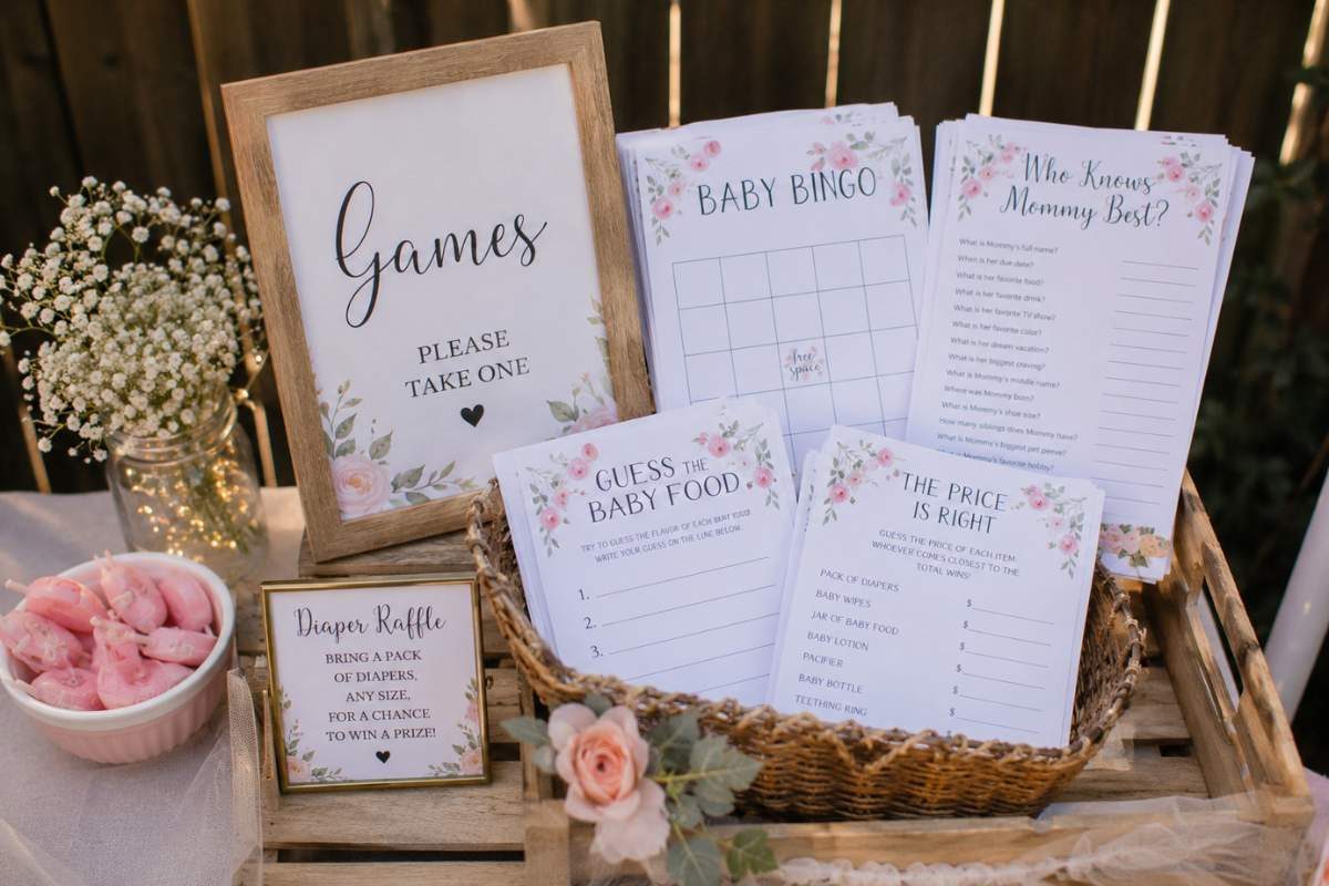Rustic baby shower game station featuring printable Baby Bingo, Guess the Baby Food, Who Knows Mommy Best, and Diaper Raffle cards displayed in a wooden crate with floral decorations and a games sign.