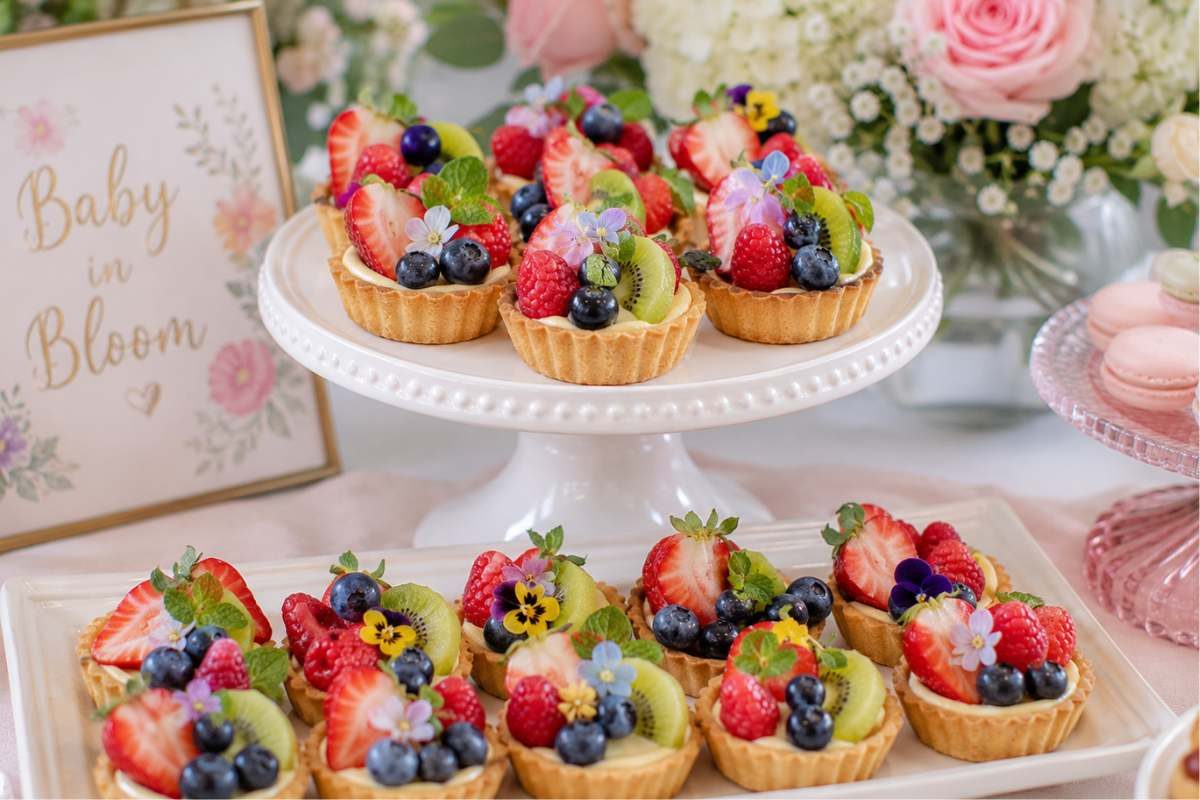 Fresh seasonal fruit tartlets topped with strawberries, blueberries, kiwi, raspberries, and edible flowers for a colorful baby shower dessert.