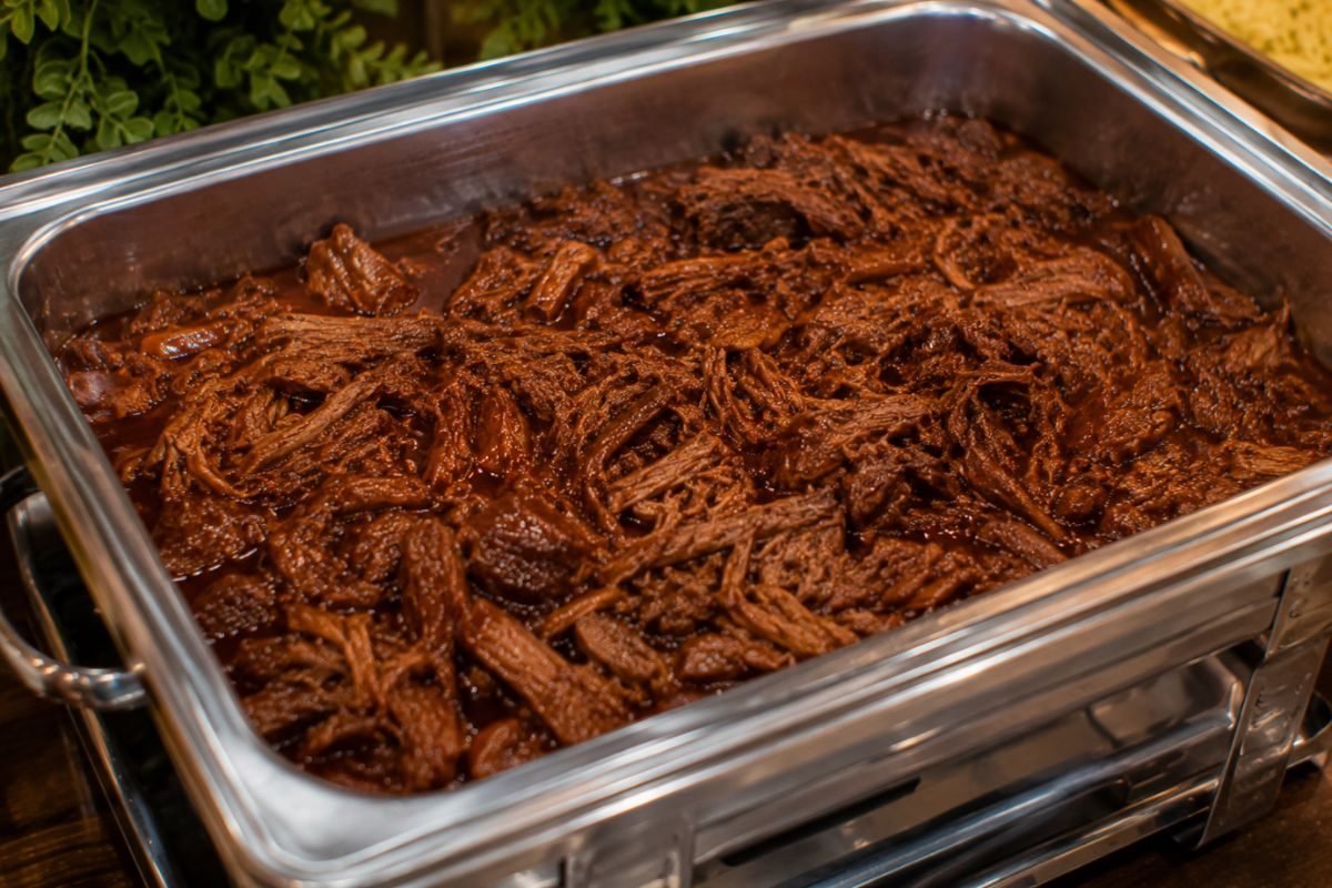 Slow-cooked barbecue beef in rich smoky sauce served in a stainless steel buffet chafing dish, offering a tender and budget-friendly entrée for a wedding reception.