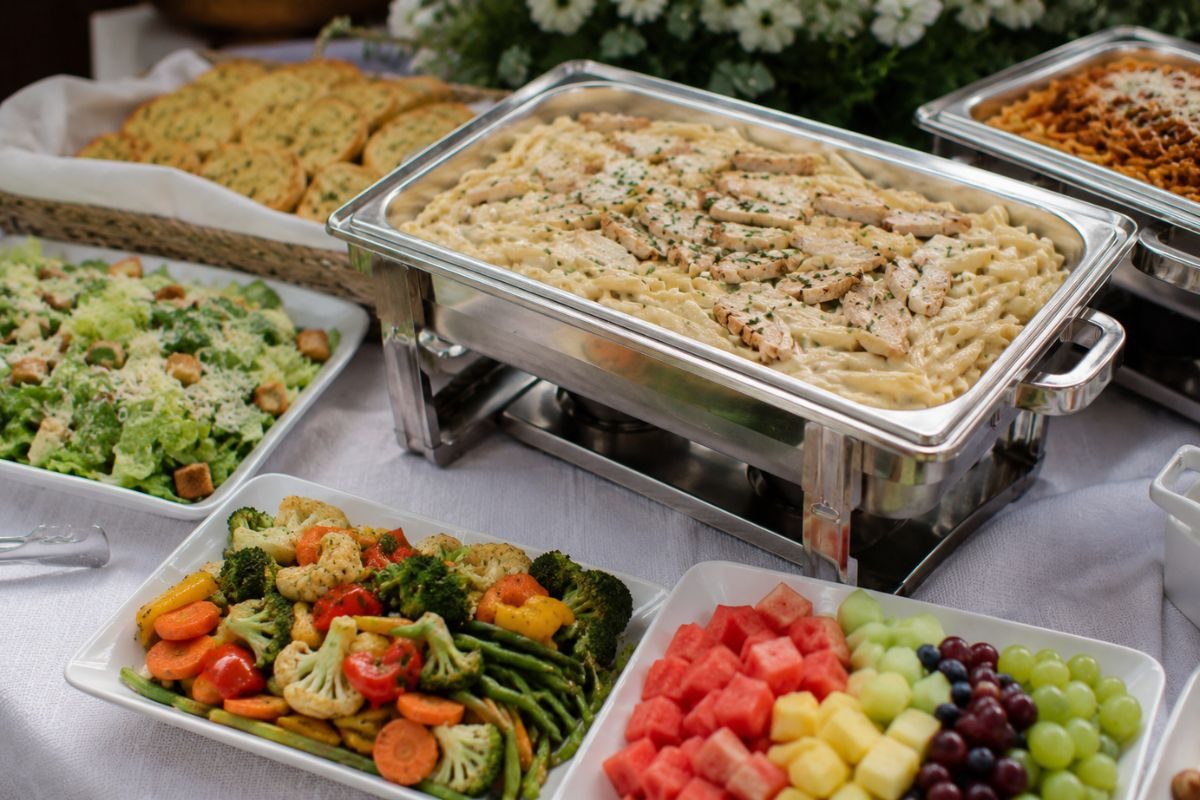 Wedding buffet featuring creamy chicken pasta served with Caesar salad, garlic bread, roasted vegetables, and fresh fruit, creating a balanced and budget-friendly reception meal.