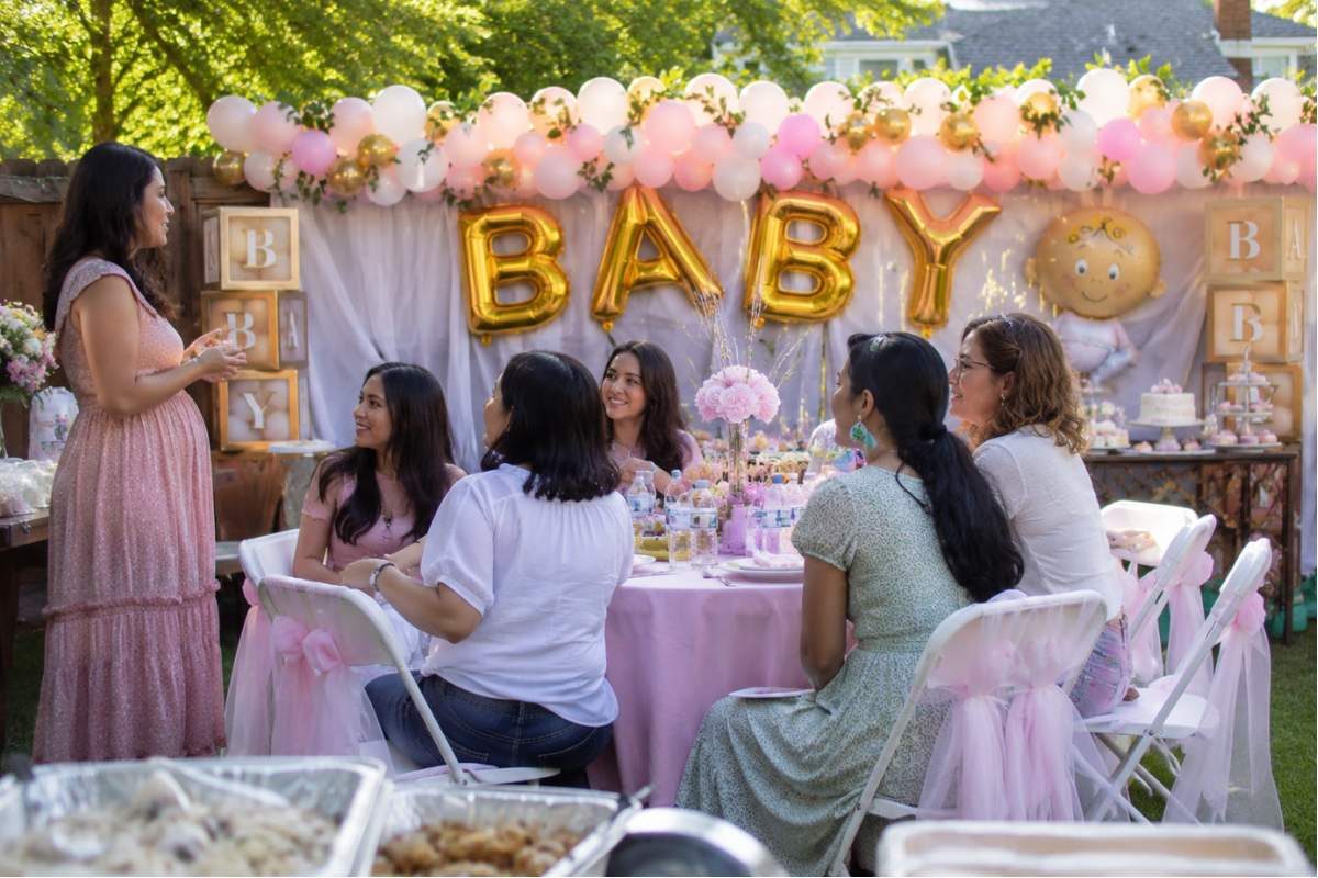Pregnant mom celebrating with family and friends at a beautifully decorated backyard baby shower featuring pastel balloons, elegant tables, and natural outdoor lighting.